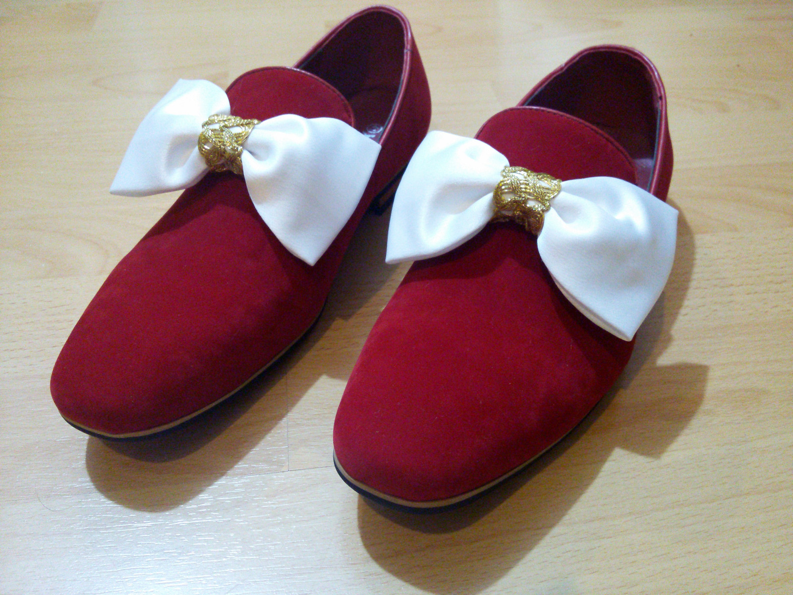 Bild: Schuhe aus rotem Velourleder, mit Schleifen aus weißem Satin und goldener Borte verziert.
